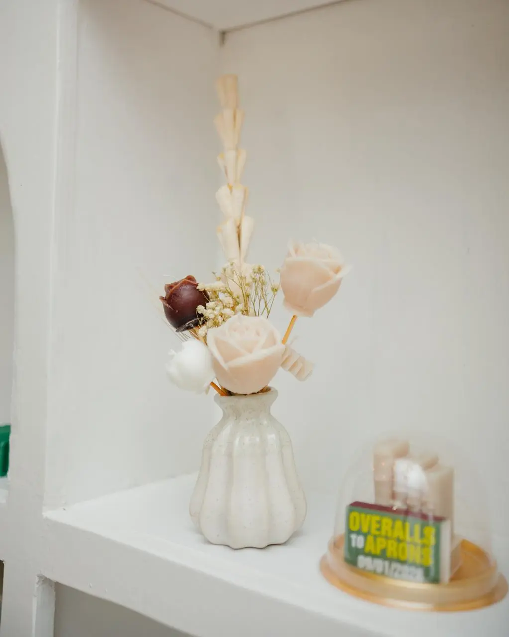 Vase filled with cream and brown rose-shaped candles on a bookshelf.